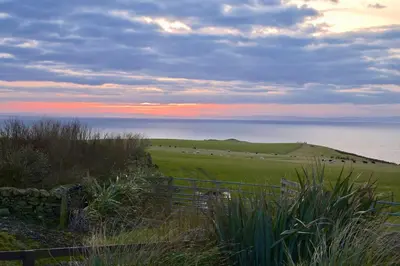 a view of a field with a fence and the ocean at Amazing Sunsets and Sea Views - Lodge Cabin Farm Stay - Caol Ila - Lodge 8 in Stranraer