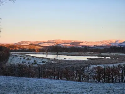 a snow covered field with a pond with mountains in the background at Morton Mains Cottage