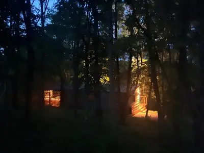 a cabin in the woods at night with the lights on at Ty Cwtch Cabin - secluded woodland cabin & covered hot tub in Moffat