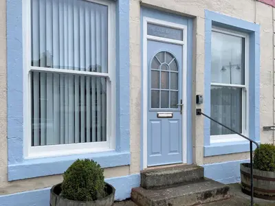 a blue door on a house with two windows at Pass the Keys Cosy Romantic Getaway with Hot Tub in Whithorn