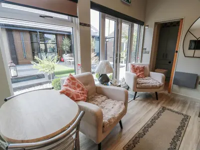 a living room with a table and chairs and large windows at Cabin At The Brig in Annan