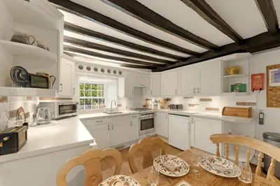 a kitchen with white cabinets and a table and chairs at Walthwaite How Cottage in Chapel Stile