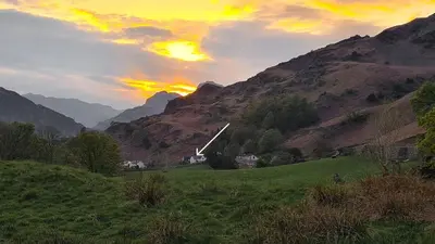 a sunset over a field with a church in the mountains at Walthwaite How Cottage in Chapel Stile