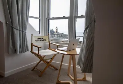 a desk with a laptop and a chair in front of a window at Moir Cottage in Portpatrick