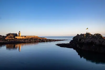 a beach with a lighthouse and a flag in the water at Moir Cottage in Portpatrick