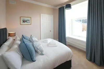 a bedroom with a bed with blue pillows and a window at Mariners Haven in Troon in Troon