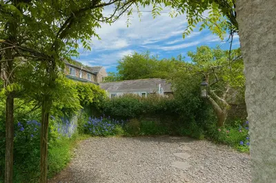 a garden with blue flowers and a house in the background at Feather Bed Cottage - Dog Friendly Lakeland Retreat with Log Burner & Garden