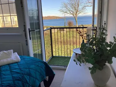 a bedroom with a balcony with a view of the water at Seascape - a Luxury Retreat on the Sea in Moffat