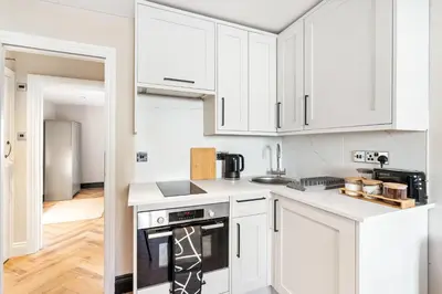 a white kitchen with white cabinets and a stove at Newly Renovated 1BR Steps from Hove Beach in Moffat