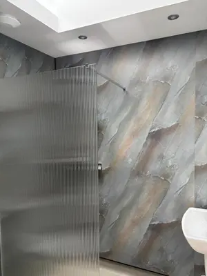 a shower in a bathroom with a stone wall at Cross Beck Cottage in Allonby