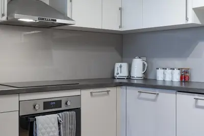 a kitchen with white cabinets and a stove top oven at Modern 2-Bed Flat with Balcony and Free Parking - Ideal for Contractors in Moffat