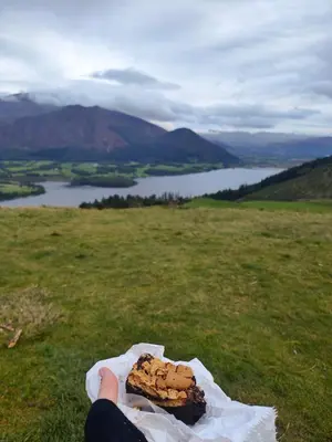 a person holding a piece of food in a field at Cozy cottage at the base of Sale and Ling Fell in Embleton