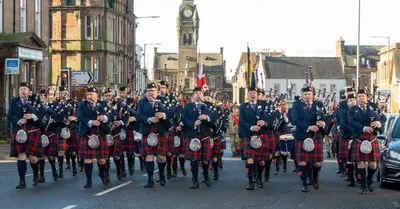 a group of men in tartan kilts marching down a street at River View Cottages in Annan