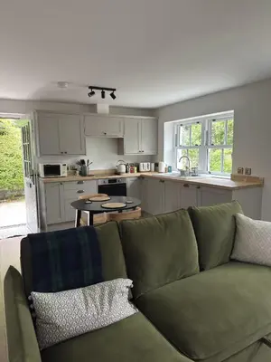 a living room with a green couch and a kitchen at Cosy Cottage in Charming Village Close to Beach - Pass the Keys in Kirkbean
