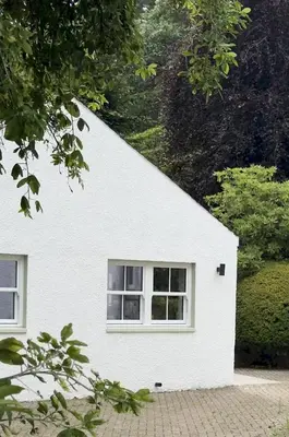 a white house with a window and trees at Cosy Cottage in Charming Village Close to Beach - Pass the Keys in Kirkbean