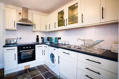 a kitchen with white cabinets and a washing machine at Cosy Cottage on edge of Lake District in Little Broughton