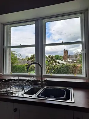 a kitchen sink with two windows above a kitchen counter at Cosy Cottage in Moffat, South Scotland in Moffat