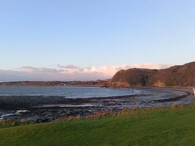 a beach with a grassy field and the ocean at 'Sunset Lodge' Peaceful Coastal Retreat with Hot Tub in Monreith