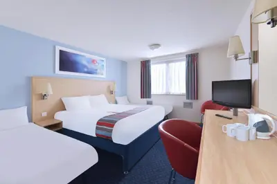 a hotel room with two beds and a chair at Travelodge Dumfries in Collin