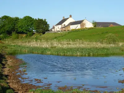 a house on top of a hill next to a pond at Milecastle, Irthington on Hadrians Wall in Irthington
