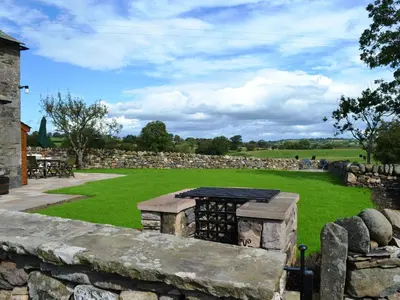 a stone fireplace in a field with a stone wall at Crofthead in Hesket Newmarket
