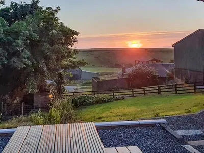 a sunset over a farm with a fence and a bench at Dairy Cottage in Girvan
