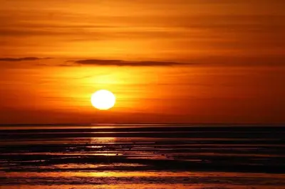 an orange sunset over the ocean with the sun in the sky at Paws A While in Mainsriddle