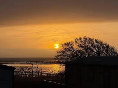 a sunset over a body of water with the sun at Paws A While in Mainsriddle