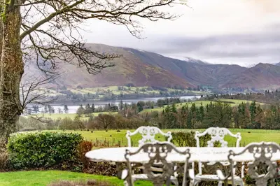 two white chairs and a table in a field at Wreay Lodge - Fellside Home with Lake Views in Watermillock