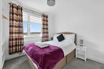 a bedroom with a bed with a purple blanket and a window at Troon Golf by the Sea in Troon