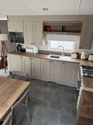 a kitchen with white cabinets and a sink and a table at Paws a while in Mainsriddle