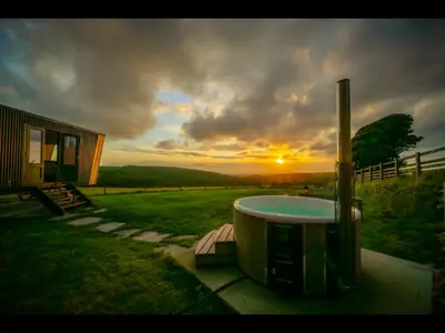 a hot tub in a yard with the sunset in the background at Laverock How Shepherds Hut with private hot tub in Seascale