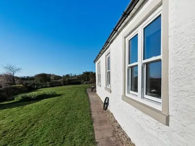 a white building with a window and a grass field at Bankswood Cottage in Ruthwell