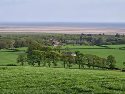 a field with trees and a castle in the distance at Bankswood Cottage in Ruthwell