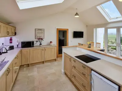 a large kitchen with wooden cabinets and a window at Bankswood Cottage in Ruthwell