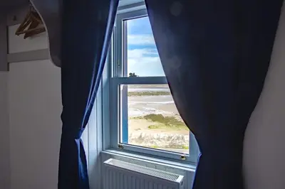 a window with a blue curtain and a view of a beach at The Harbour Inn in Garlieston