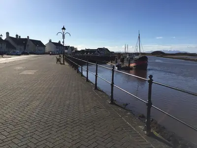 a walkway next to a river with a boat in the water at Irvine Bay in Irvine