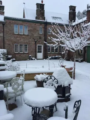 a yard covered in snow with chairs and a building at Beech House in Greystoke