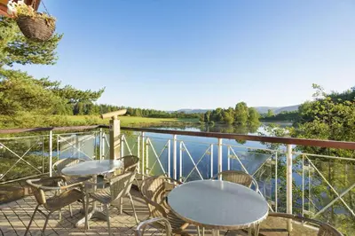 a balcony with tables and chairs and a view of a river at Days Inn Lockerbie - Annandale Water in Johnstonebridge