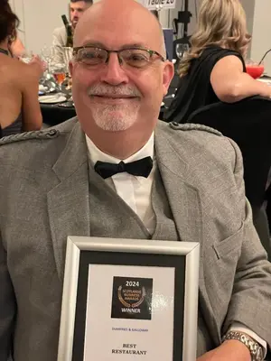 a man in a suit holding an award trophy at The Ship Inn - Winner Best Hotel Experience 2024 Visit Scotland in Gatehouse of Fleet