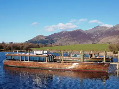 a boat is docked on the water with mountains in the background at Chaucers Nook in Keswick