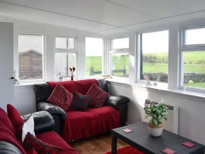 a living room with a red couch and windows at Wee Dug Hoose in Glenluce