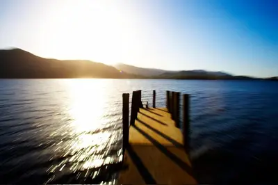 a dock on a body of water with the sun setting at Ann's Hill in Cockermouth