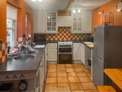 a kitchen with white cabinets and an orange wall at Bay Cottage in Keswick