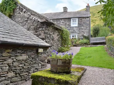 a stone house with purple flowers in front of it at Ingle Neuk Cottage in Mosedale