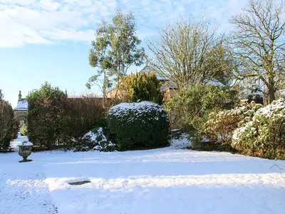 a yard covered in snow with bushes and trees at Gilminscroft Gatehouse in Sorn