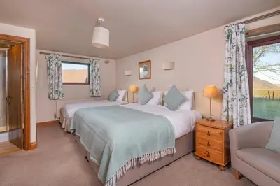 a bedroom with two beds and a chair and a window at Saddleback Barn in Penrith