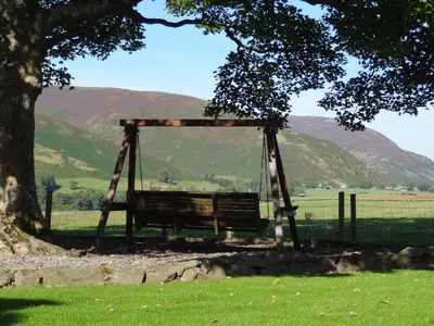 a wooden swing under a tree in a field at Stable Barn in Penrith