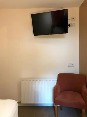 a room with a chair and a television on the wall at Glenlossie Guest House in Dumfries