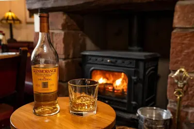a bottle of whisky and a glass on a table with a fireplace at Royal Hotel in Dockray